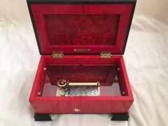 red music box open with black feet and trim showing the gold inner workings of the musical box