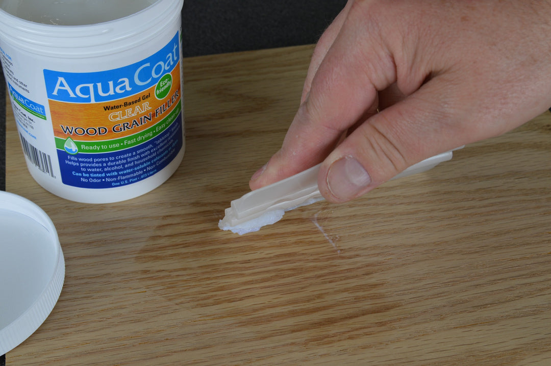 Aqua Coat Grain Filler on the left hand side in a white tub sitting on a piece of wood while someone applies the filler