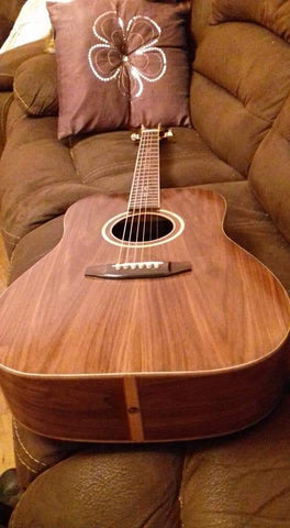 acoustic guitar in medium brown wood finish sitting on a brown couch