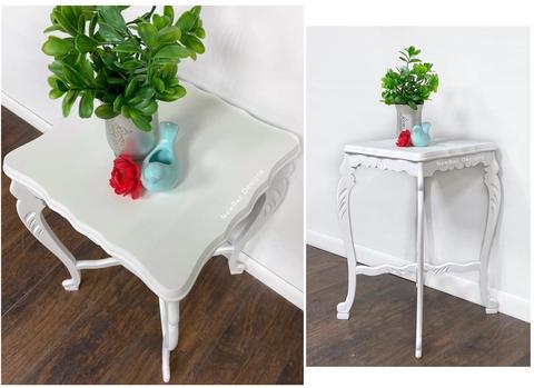 White side table with a plant a rose and a blue bird ceramic on it