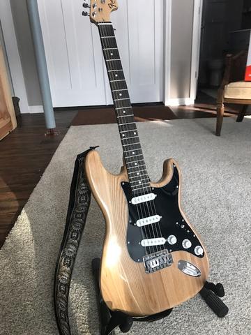 custom Guitar with light wood finish and a black strap