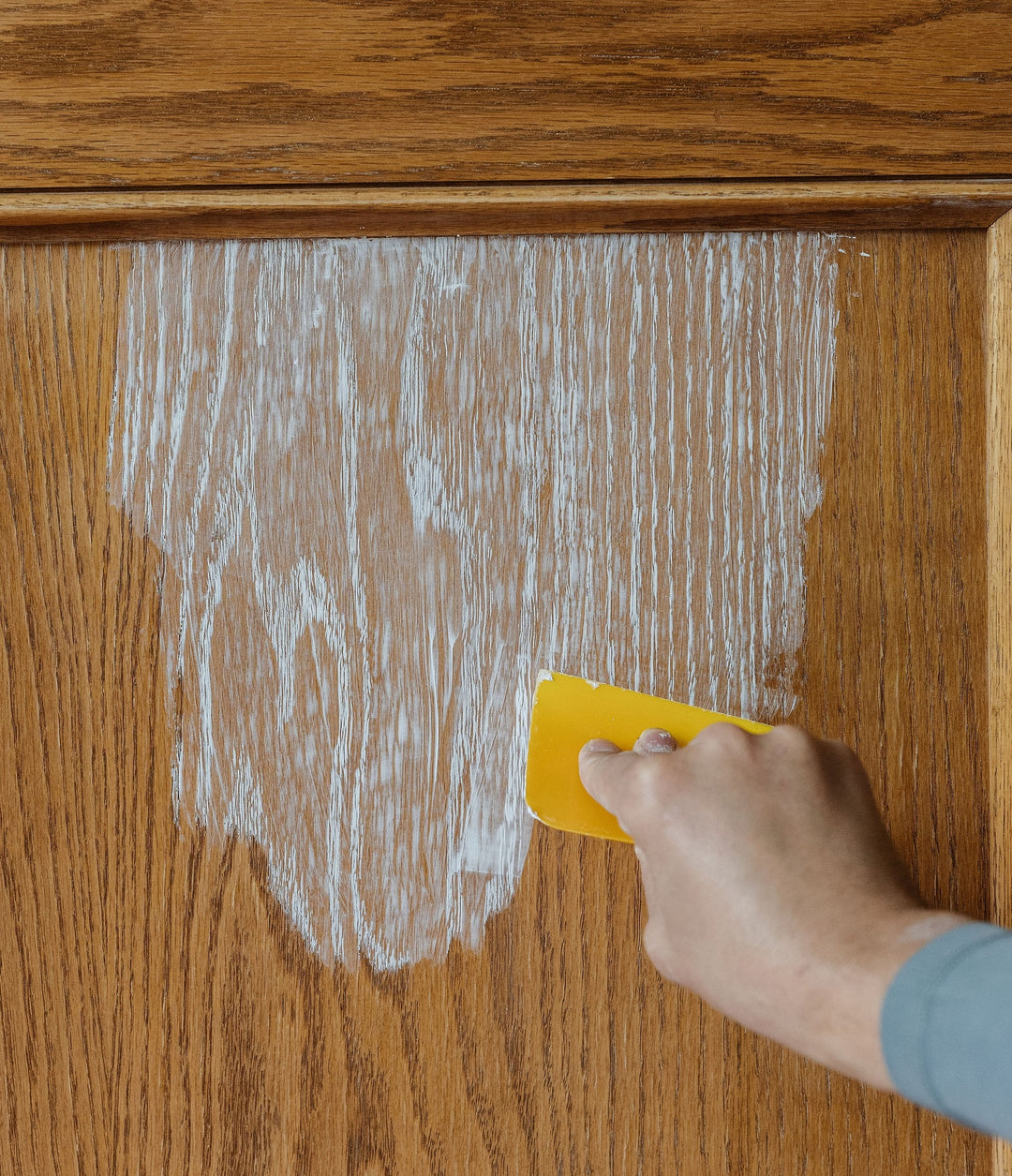 wood cabinet with aqua coat white grain filler being applied using a yellow squeegee