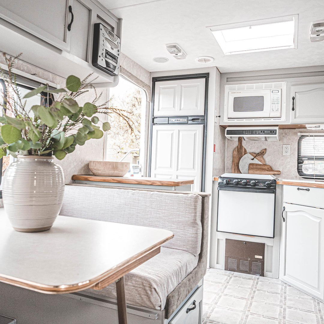 photo taken in a Remodeled camper showcasing white cabinetry white appliances and a white table with a plant on it in a white vase
