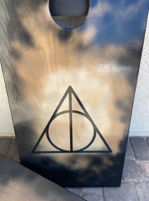 cornhole board showcasing the deathly hollows symbol from harry potter in black with a wood to black gradient background