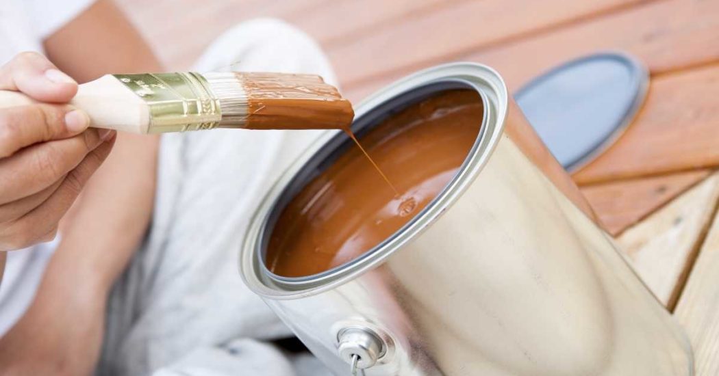 can of paint with paint brush dripping into it in a brown-orange color