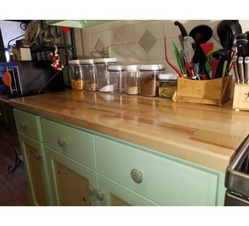 kitchen cabinet with light green paint and a light grain wood butcher block top with utensils and spices on the counter